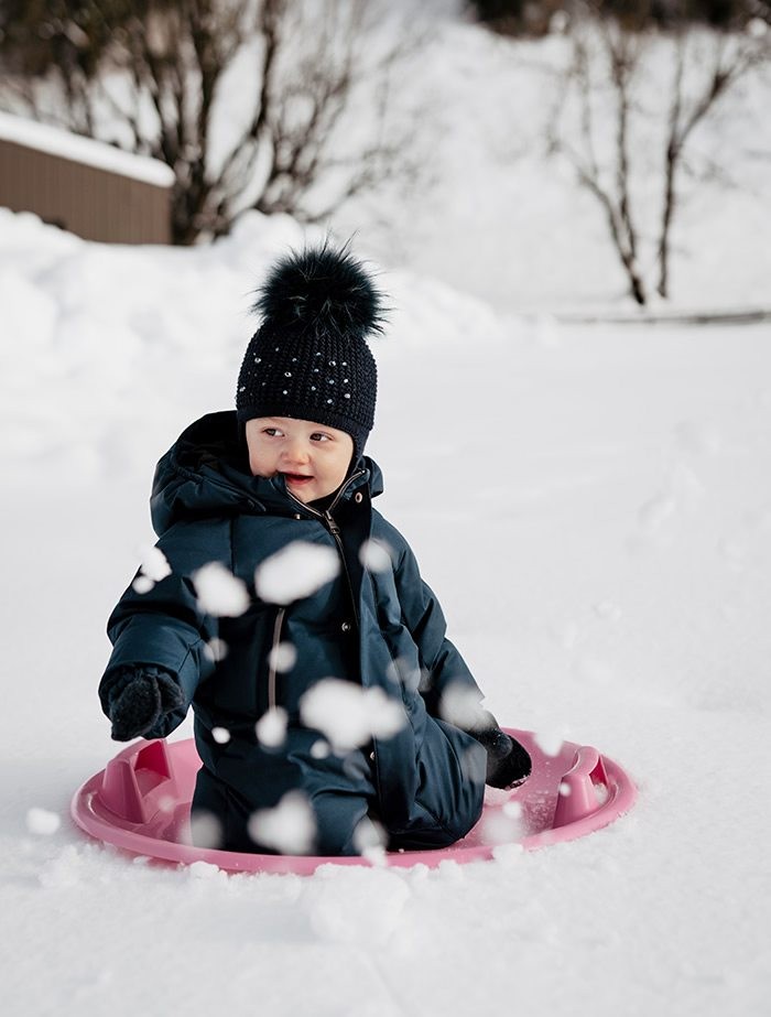 Kind auf einem Rutschblatt im Winter